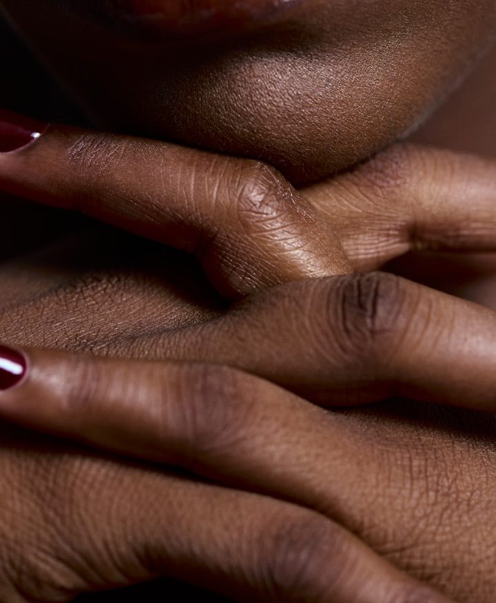 Massage + Essen Detailaufnahme von gekreuzten Händen mit rotem Nagellack auf dunkelbrauner Haut.